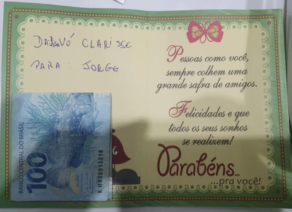 Cartão verde endereçado pela Bisa Vó Clarisse ao Jorge, com uma nota de R$ 100 sobre ele.